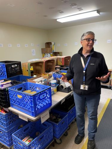 Casey Davis stands in front of a table stacked with blue crates in one of the Edmonds Food Bank store rooms.
