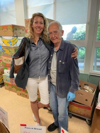 Shilo poses with her grandfather Tom in front of boxes of food at the Edmonds Food Bank.